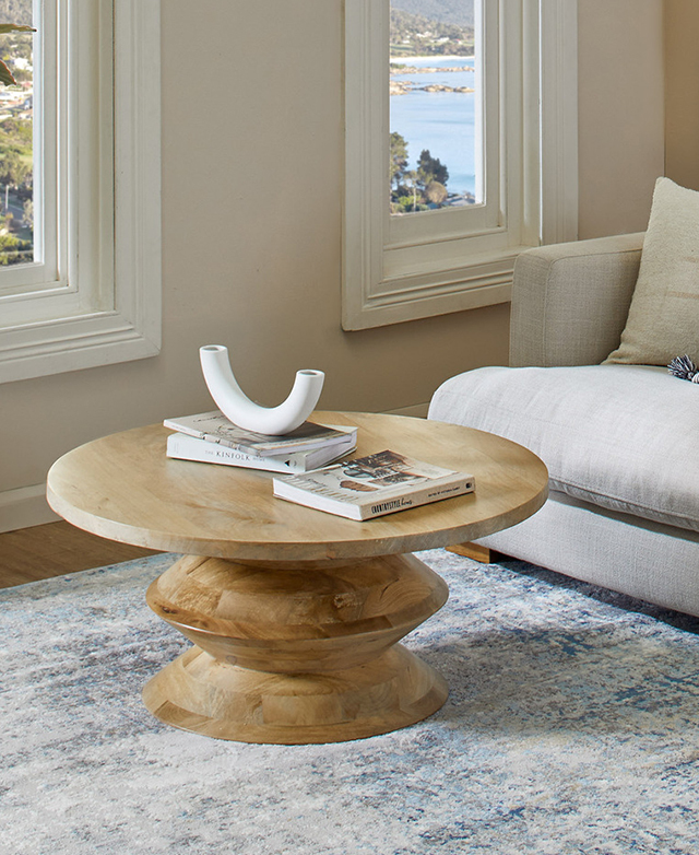 Coffee table is displayed in a bright living room on top of a blue, abstract rug. Books and a ceramic sculpture are on top. Coffee table is displayed in a bright living room on top of a blue, abstract rug. Books and a ceramic sculpture are on top.