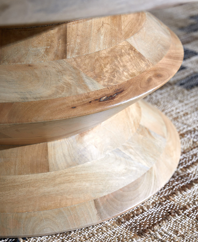 Close up of the coffee table's base, which has a sculptural form and is made from warm-hued mango wood. Close up of the coffee table's base, which has a sculptural form and is made from warm-hued mango wood.