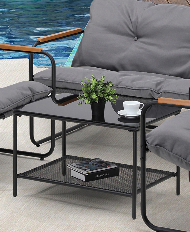 The black glass and metal coffee table is in focus, shown with books on the mesh shelf and a plant on the top.