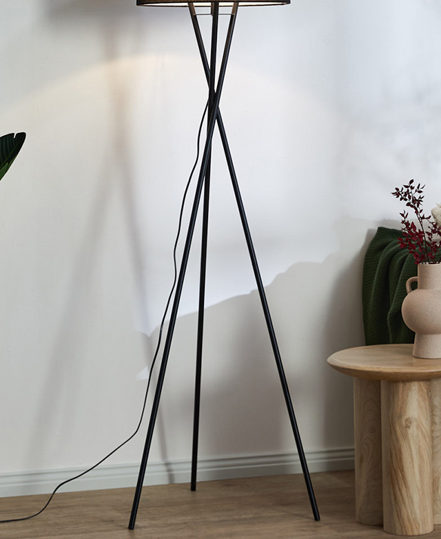 Contemporary black metal tripod lamp base has long, slender legs, positioned in front of a white wall and casting shadows. Contemporary black metal tripod lamp base has long, slender legs, positioned in front of a white wall and casting shadows.