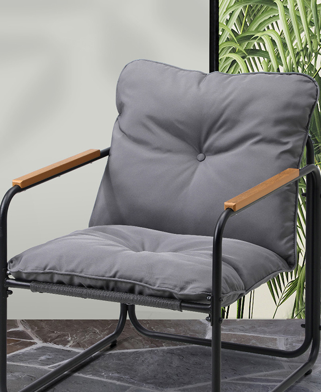 The wide grey chair is positioned at an angle on grey-toned outdoor tiles.