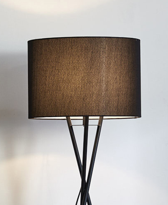 A black fabric drum shade is on top of an illuminated black floor lamp, which is emitting a soft glow. A black fabric drum shade is on top of an illuminated black floor lamp, which is emitting a soft glow.