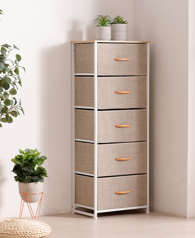 A cream tallboy is positioned in the corner of a room, with pot plants on top and nearby.