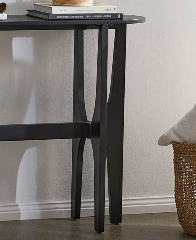 At once angular, curved, and tapered, the legs of the console table are shown in front of a white wall, casting shadows. At once angular, curved, and tapered, the legs of the console table are shown in front of a white wall, casting shadows.