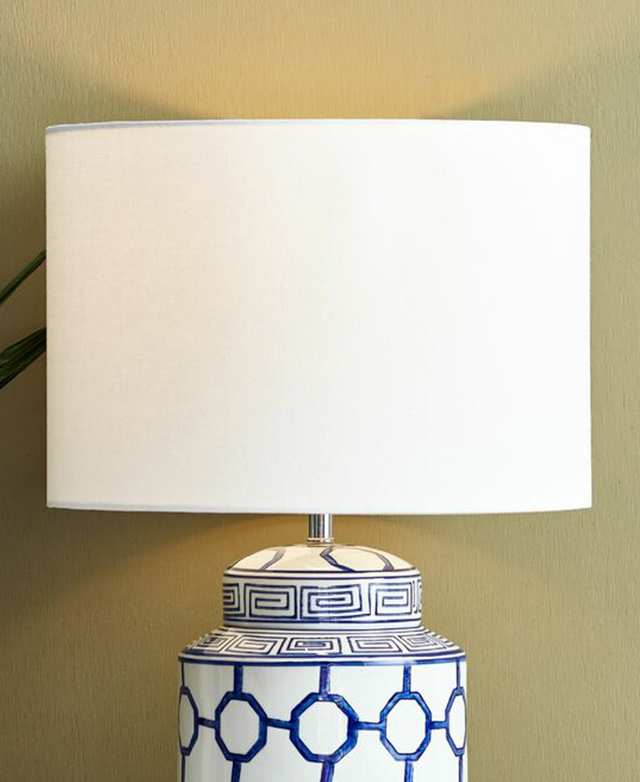 A white fabric drum shade tops a blue and white ceramic lamp base, in front of a green wall. A white fabric drum shade tops a blue and white ceramic lamp base, in front of a green wall.