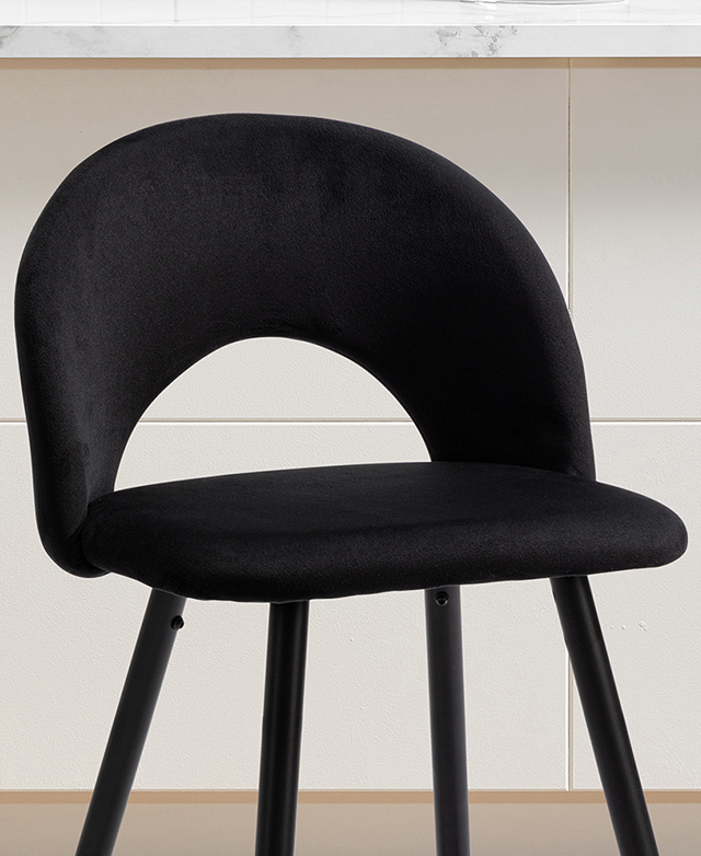 A black velvet bar stool has a rounded seat and mid-height backrest, and it's next to a white counter. A black velvet bar stool has a rounded seat and mid-height backrest, and it's next to a white counter.