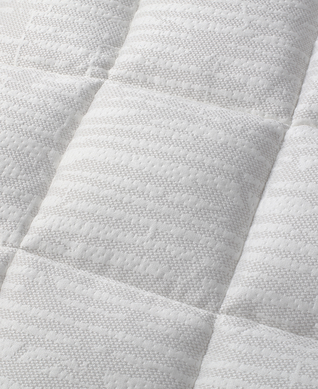 The topper's surface is zoomed in on to show the box-stitch construction and the woven texture of the white fabric.