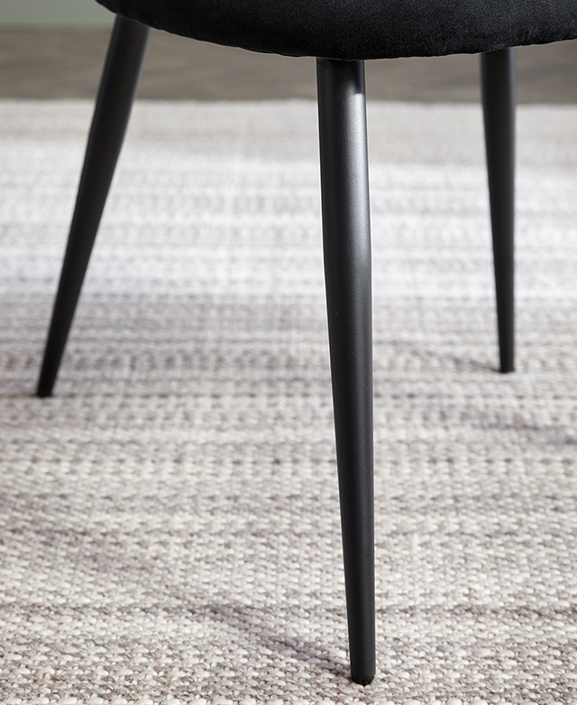 Focus is on the dining chair's front leg, which is slender, tapered, black metal.