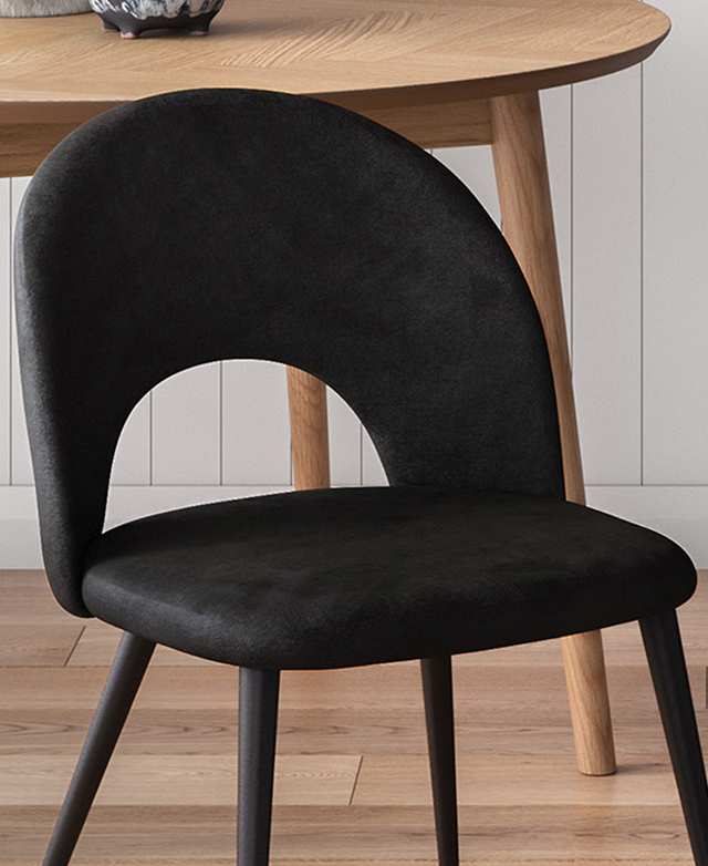 A black velvet dining chair has a rounded seat and mid-height backrest, and it's next to a timber dining table.