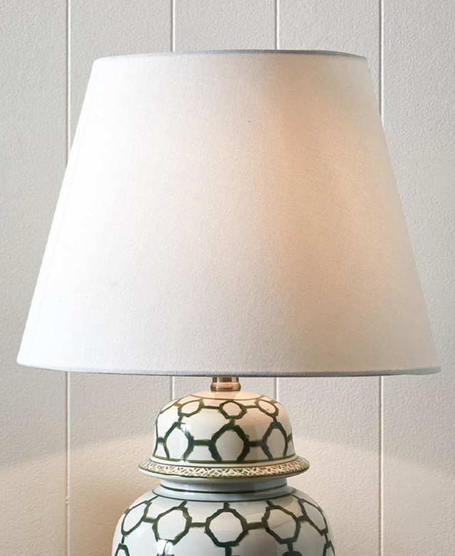 Fabric empire shade, in white, is positioned in front of an off-white panelled wall. Fabric empire shade, in white, is positioned in front of an off-white panelled wall.