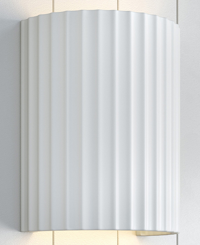 A white, fluted, semi-circular wall light is attached to a panelled wall with light being thrown from the top and bottom. A white, fluted, semi-circular wall light is attached to a panelled wall with light being thrown from the top and bottom.