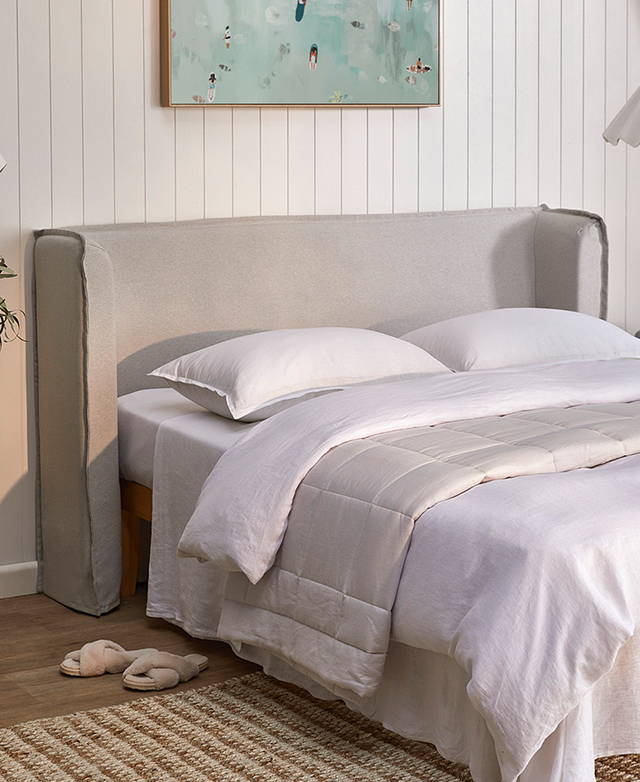 The bedhead is propped up behind a bed, which is draped in layers of white and off-white bedding.