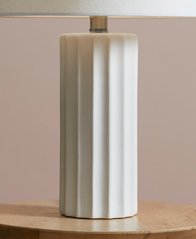 The fluted ceramic base is on a timber side table; shadows are cast over the lamp base. The fluted ceramic base is on a timber side table; shadows are cast over the lamp base.