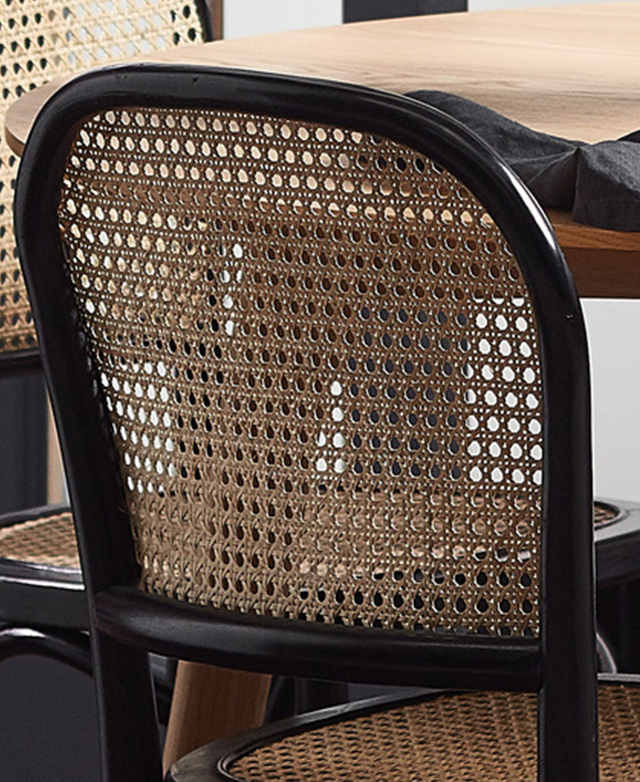 The back of a black and natural rattan dining chair is shown next to a timber dining table.