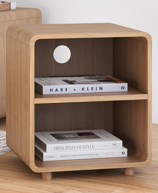 On a similarly coloured timber floor, the boxy side table is shown with white books on its open shelves. On a similarly coloured timber floor, the boxy side table is shown with white books on its open shelves.