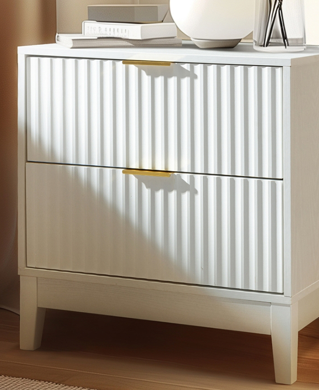 A shadow is cast over the fluted front of the white drawers, while various decorative items are stacked on top.