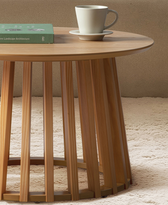 A green book and a white cup and saucer are on top of the round coffee table, which is on a high-pile, cream rug. A green book and a white cup and saucer are on top of the round coffee table, which is on a high-pile, cream rug.