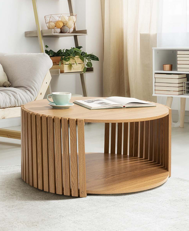 The large, round coffee table is in the centre of a living room, on top of a creamy rug and near a neutral sofa.