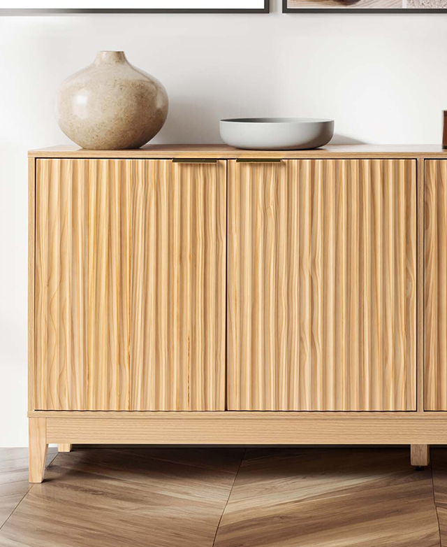 A blonde buffet is positioned against a white wall, on top of a parquet timber floor. Decorative items are on top.