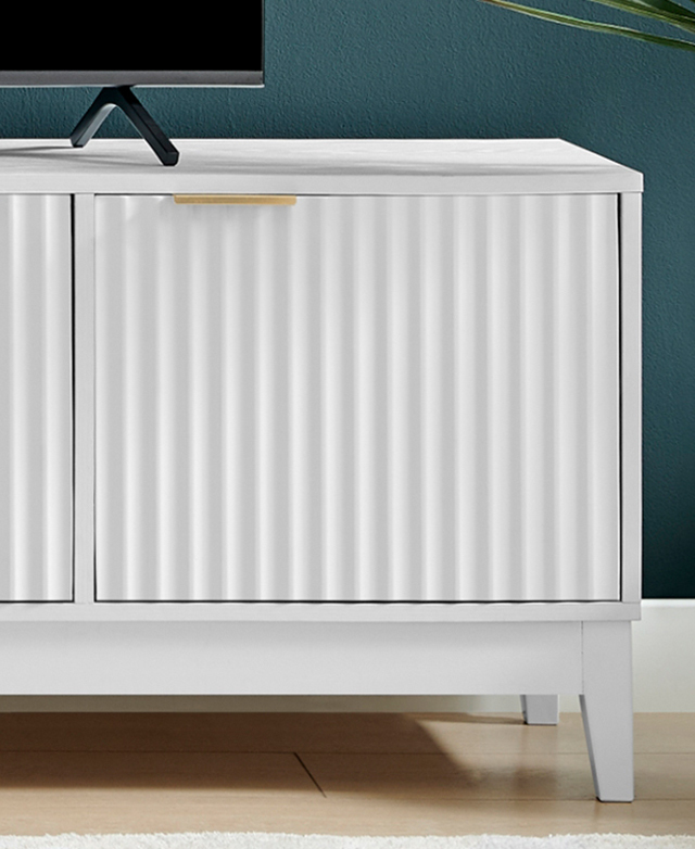 One end of the white entertainment unit against a teal wall, highlighting the fluted doors and a brass tab handle.