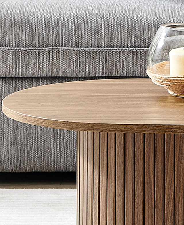 A walnut-coloured coffee table is pictured in front of a grey sofa, with a glass-protected candle on top.