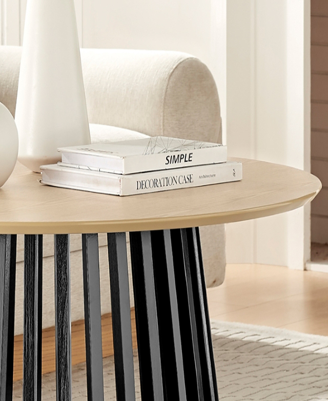 A black and natural round coffee table is shown with a stack of books and vases on top.