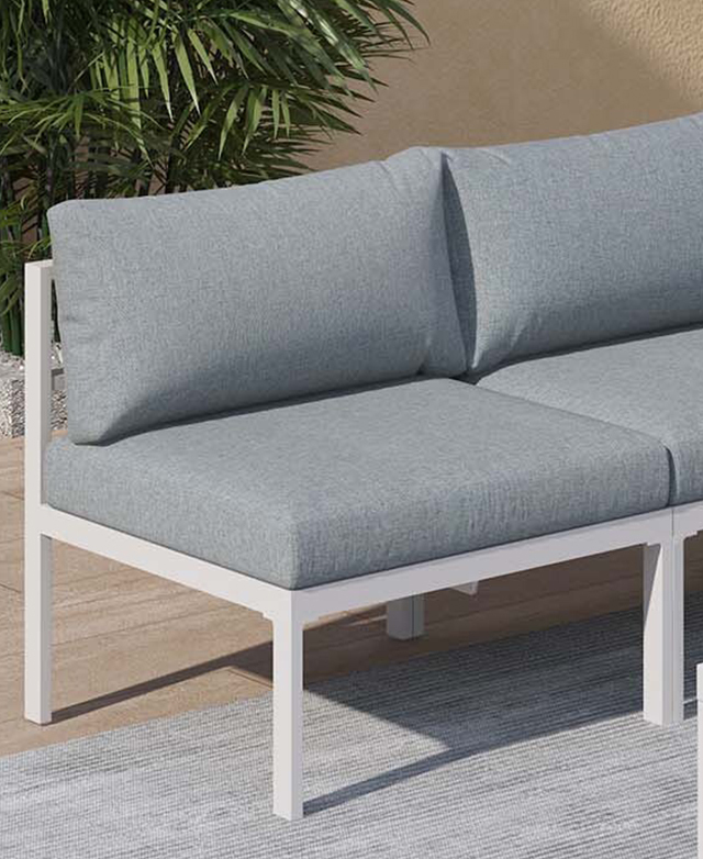 An end of the grey and white outdoor lounge is positioned on a grey rug in front of spiky green leaves. An end of the grey and white outdoor lounge is positioned on a grey rug in front of spiky green leaves.