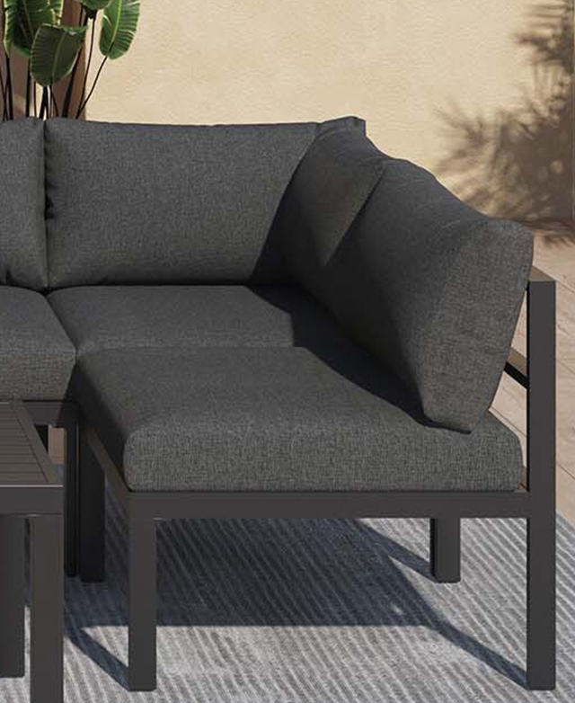 A corner section of a charcoal outdoor lounge is in a bright, sunlit area on top of a grey rug. A corner section of a charcoal outdoor lounge is in a bright, sunlit area on top of a grey rug.