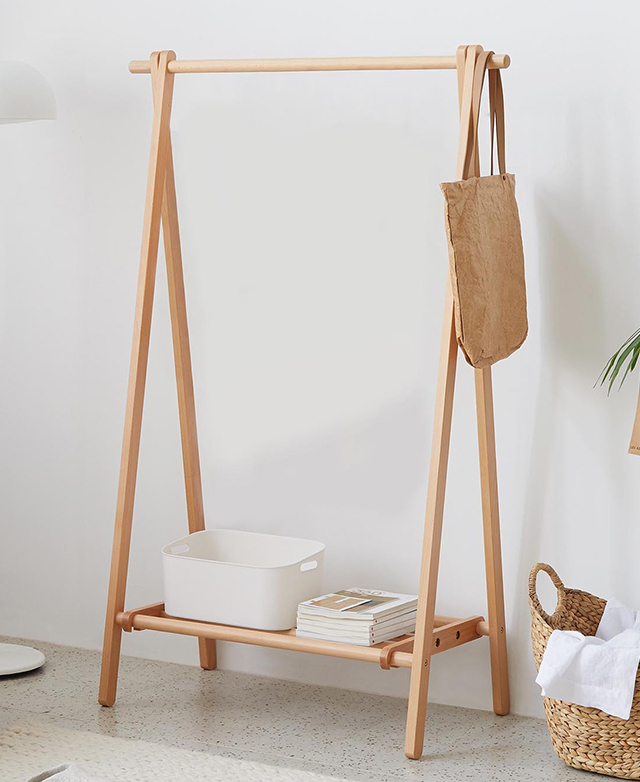 The clothing rack is positioned in a bright room against a white wall; a tub, books, and bag adorn it.