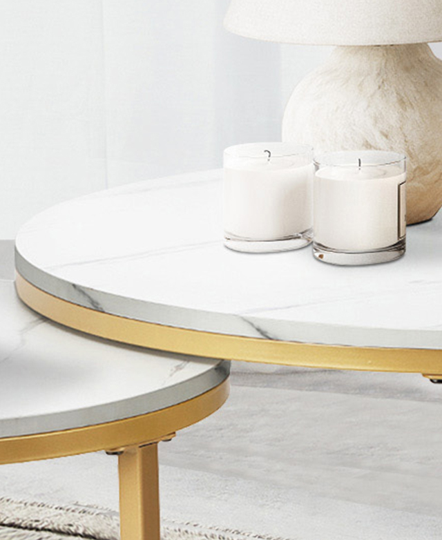 Two candles and a lamp are on top of the larger coffee table, which is layered over the shorter coffee table. Two candles and a lamp are on top of the larger coffee table, which is layered over the shorter coffee table.
