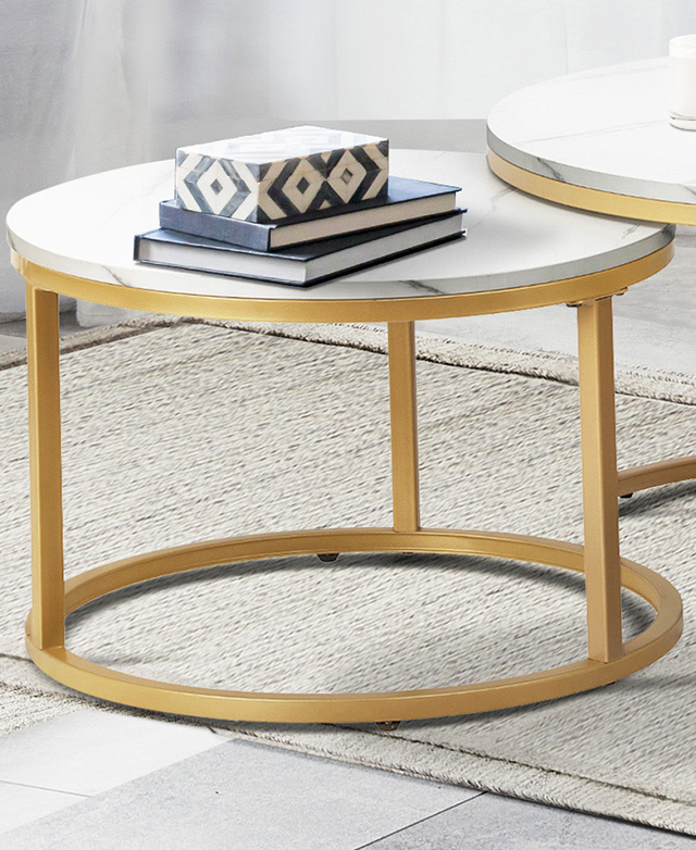 The golden metal coffee table frame is simple and open, with space beneath the white marbled surface. The golden metal coffee table frame is simple and open, with space beneath the white marbled surface.