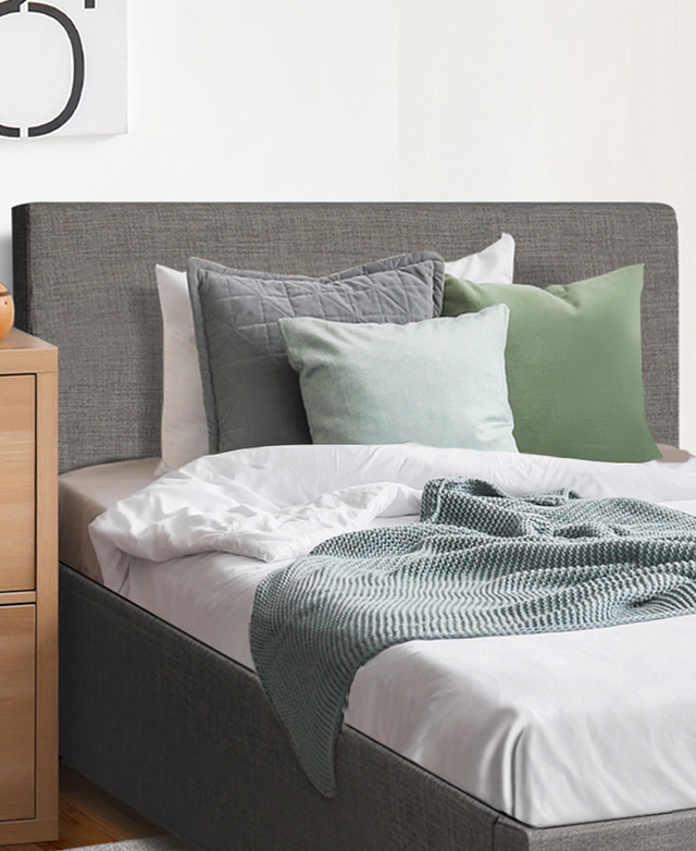 Grey upholstered bed with bedhead is in front of a white wall; the sheets are white, & cushions & throw are blue & grey. Grey upholstered bed with bedhead is in front of a white wall; the sheets are white, & cushions & throw are blue & grey.
