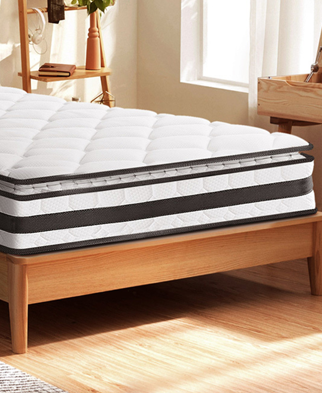 Black and white mattress is on a timber bed frame in a bright bedroom, with shelving next to the bed. Black and white mattress is on a timber bed frame in a bright bedroom, with shelving next to the bed.