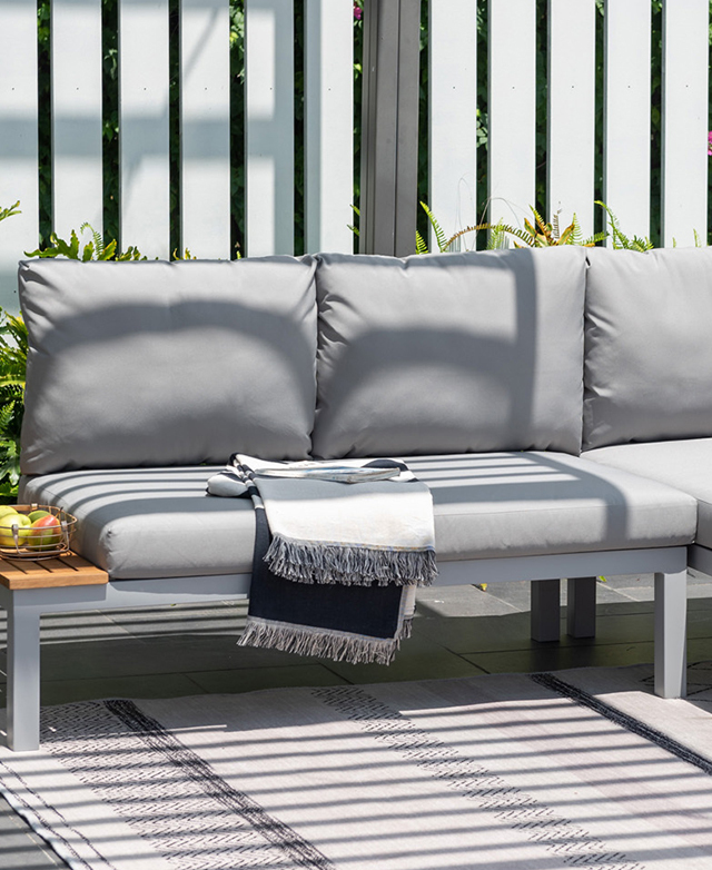 Dappled light plays across the lounge seat, which is positioned outside on top of a monochrome patterned rug.