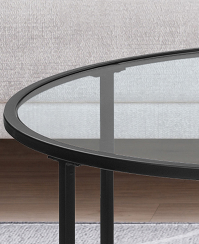 The round coffee table's glass top is transparent and shows the floor and sofa through it.