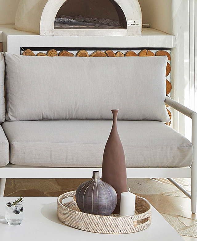 A pizza oven is in the background, a coffee table with decor in the foreground, and the white and grey sofa is the focus. A pizza oven is in the background, a coffee table with decor in the foreground, and the white and grey sofa is the focus.