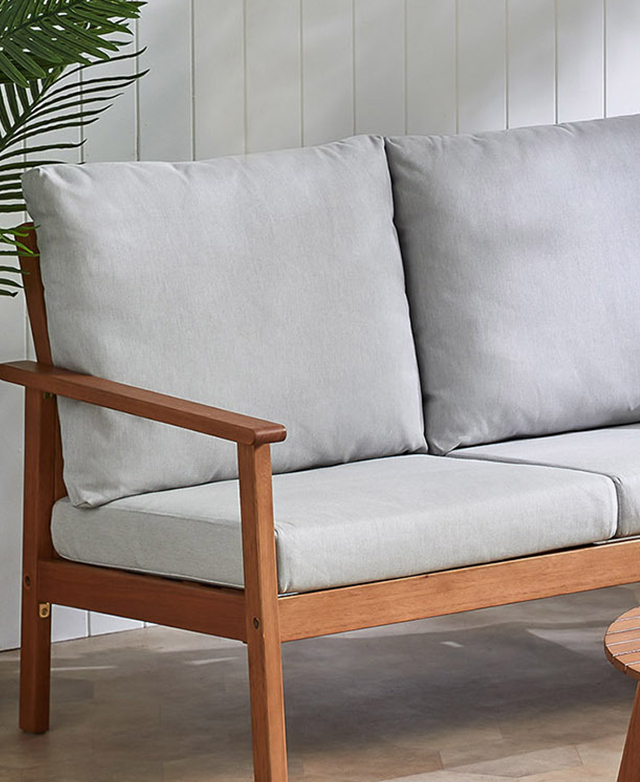The end of the sofa is shown, with its slender rich-toned timber frame and grey cushions in focus. The end of the sofa is shown, with its slender rich-toned timber frame and grey cushions in focus.