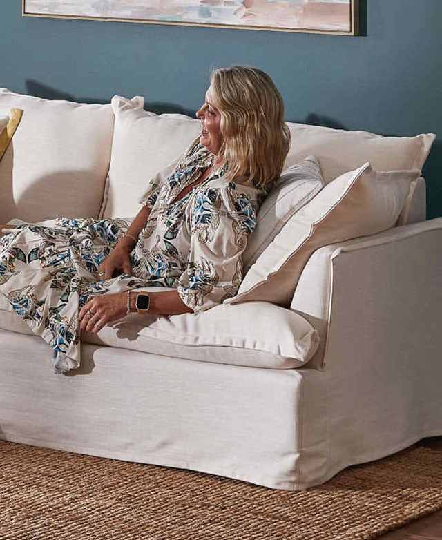 A laughing, blonde-haired woman in a blue patterned dress reclines on the cream sofa, which is on a jute rug. A laughing, blonde-haired woman in a blue patterned dress reclines on the cream sofa, which is on a jute rug.