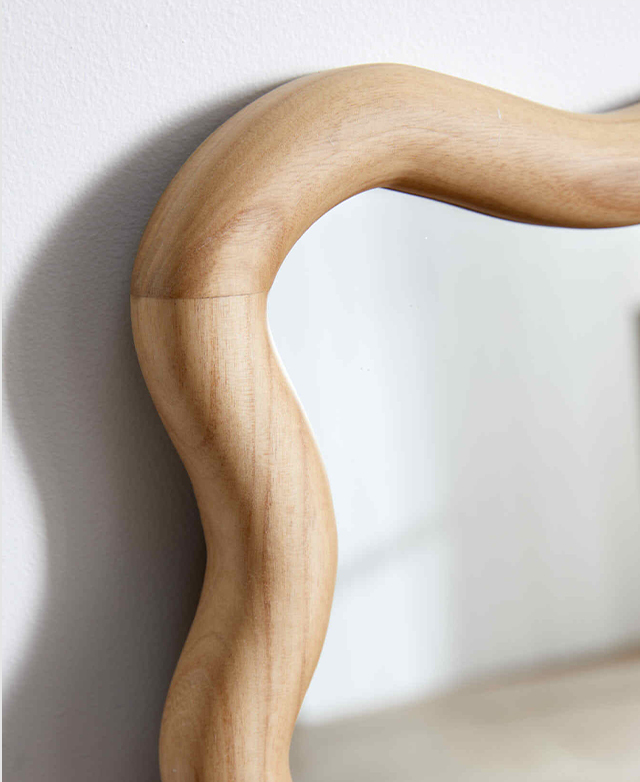 Cropped view of the mirror against a white wall, casting shadows. The natural grains of the wavy frame are in focus. Cropped view of the mirror against a white wall, casting shadows. The natural grains of the wavy frame are in focus.
