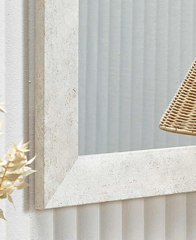 Faceted frame appears like stone with a subtle, mottled effect. Its hung on a white fluted wall.