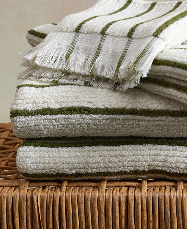 A stack of olive and cream striped bath towels with fringing is on a jute stool.