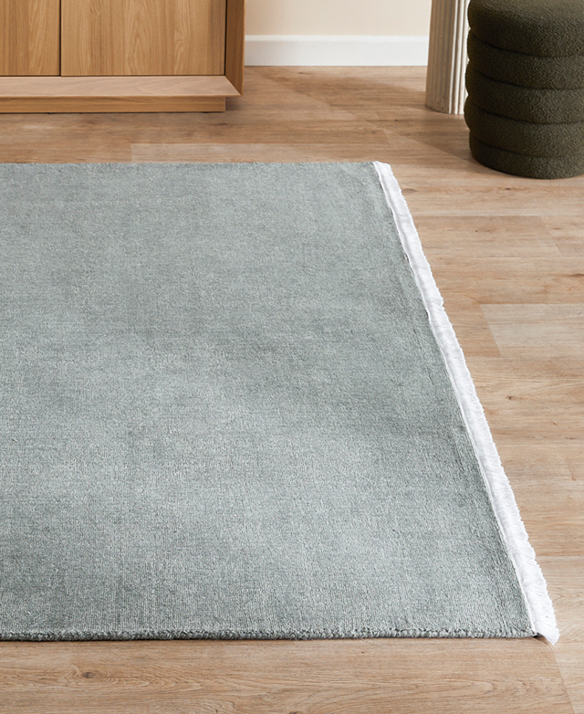 Light green wool rug has a white fringed end; it's on a light-toned timber floor.