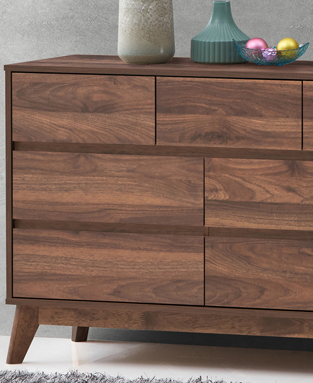 The clean lines of the walnut chest of drawers are shown close up. Decor is displayed on top.