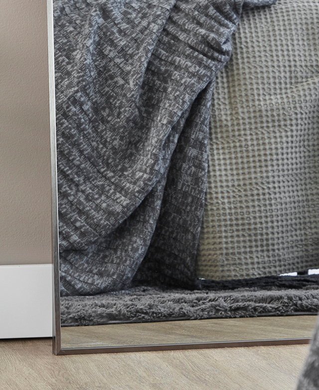 Cropped view of the bottom corner of the mirror shows it leaning against a wall and reflecting waffle and knitted throws. Cropped view of the bottom corner of the mirror shows it leaning against a wall and reflecting waffle and knitted throws.