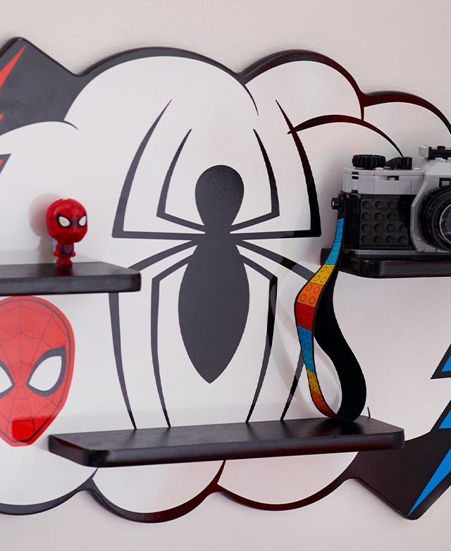 The central spider motif of the wall shelf's backdrop is framed by three shelves, which are topped with figurines. The central spider motif of the wall shelf's backdrop is framed by three shelves, which are topped with figurines.