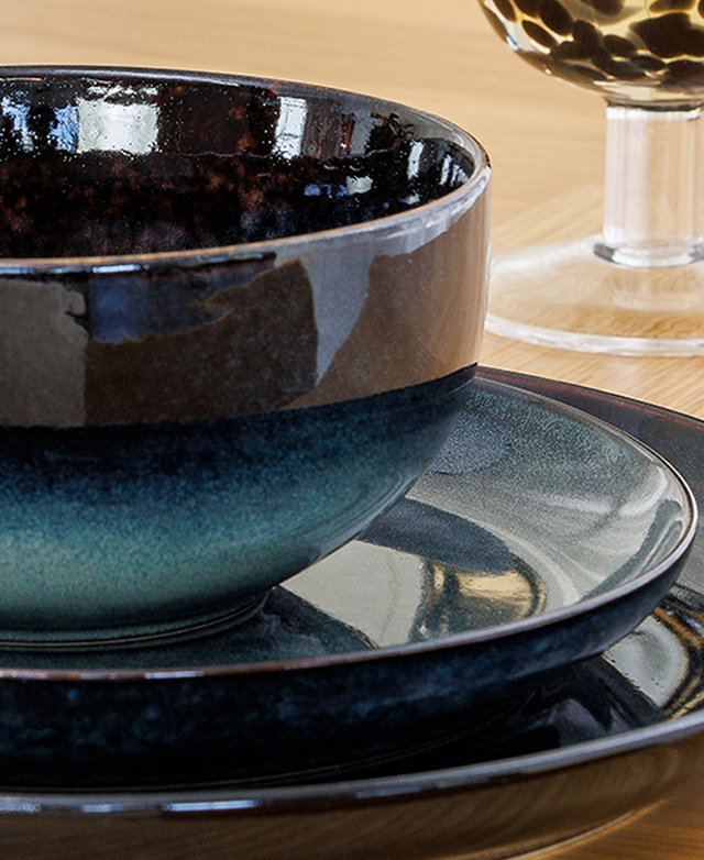 A close view of a blue bowl, side plate, and dinner plate emphasises the glossy finish of the ceramic. A close view of a blue bowl, side plate, and dinner plate emphasises the glossy finish of the ceramic.