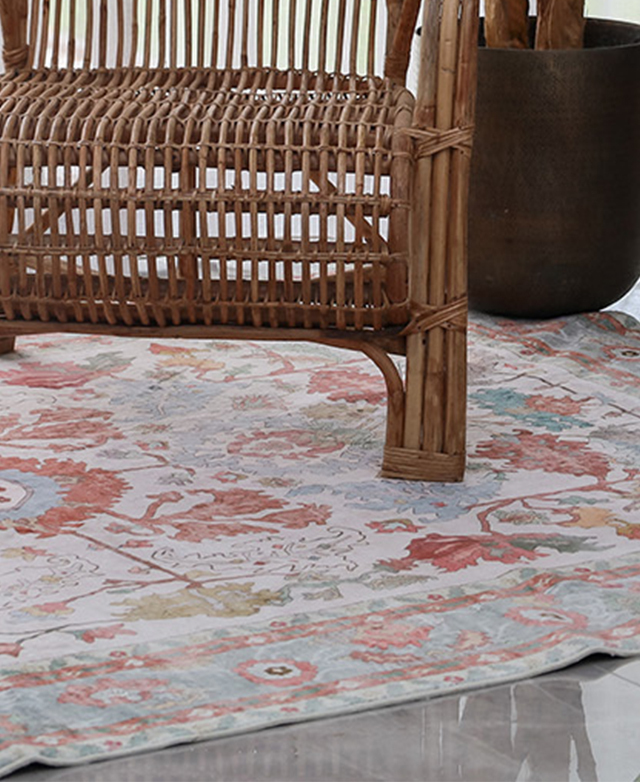 A bohemian-style rattan chair and a plant pot is on top of the colourful patterned rug.