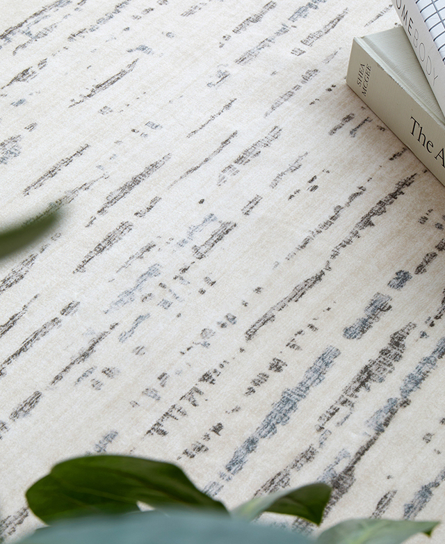 A close view of the cream, blue, and charcoal abstract pattern highlights the rug's smooth finish. A close view of the cream, blue, and charcoal abstract pattern highlights the rug's smooth finish.