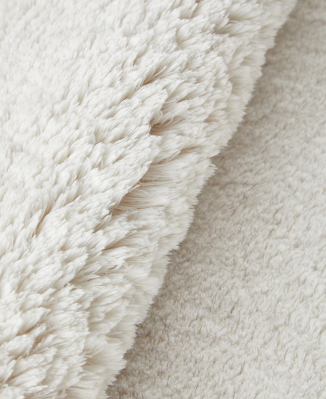 The cream rug is folded back on itself to magnify its thick pile.