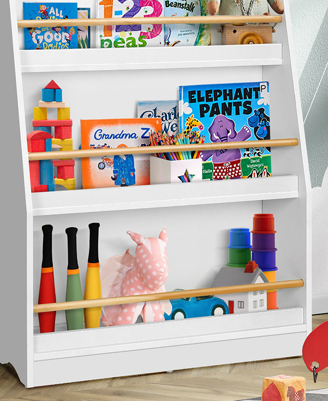 Front-facing books and several colourful toys fill the spaces of the children's white bookshelf. Front-facing books and several colourful toys fill the spaces of the children's white bookshelf.